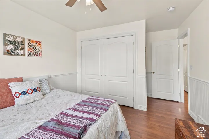 Room featuring wood-finish flooring, white beadboard wainscoting, double-door closet, and ceiling fan with integrated light fixture