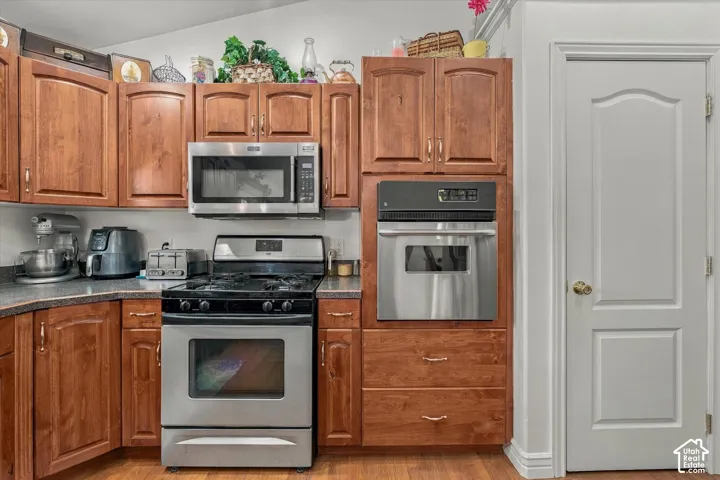 Kitchen featuring wood cabinetry, stainless steel gas range, over-the-range microwave, built-in wall oven, and dark-toned countertops