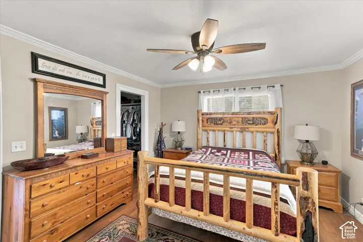 Room featuring neutral wall paint, wood-finish flooring, crown molding, and a ceiling fan with integrated lighting