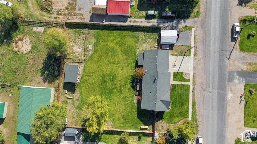 Aerial perspective of a property featuring a rectangular lot, expansive lawn, detached storage structure, and fenced perimeter