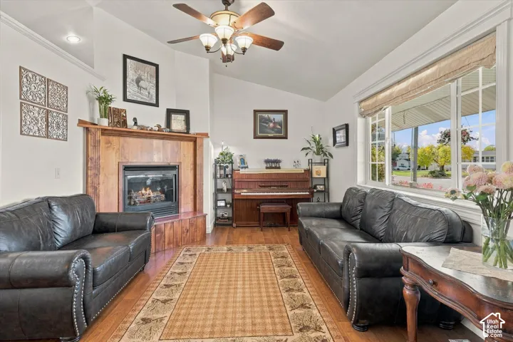 Vaulted ceiling, wood-finish flooring, corner fireplace with wood surround, and multi-pane window