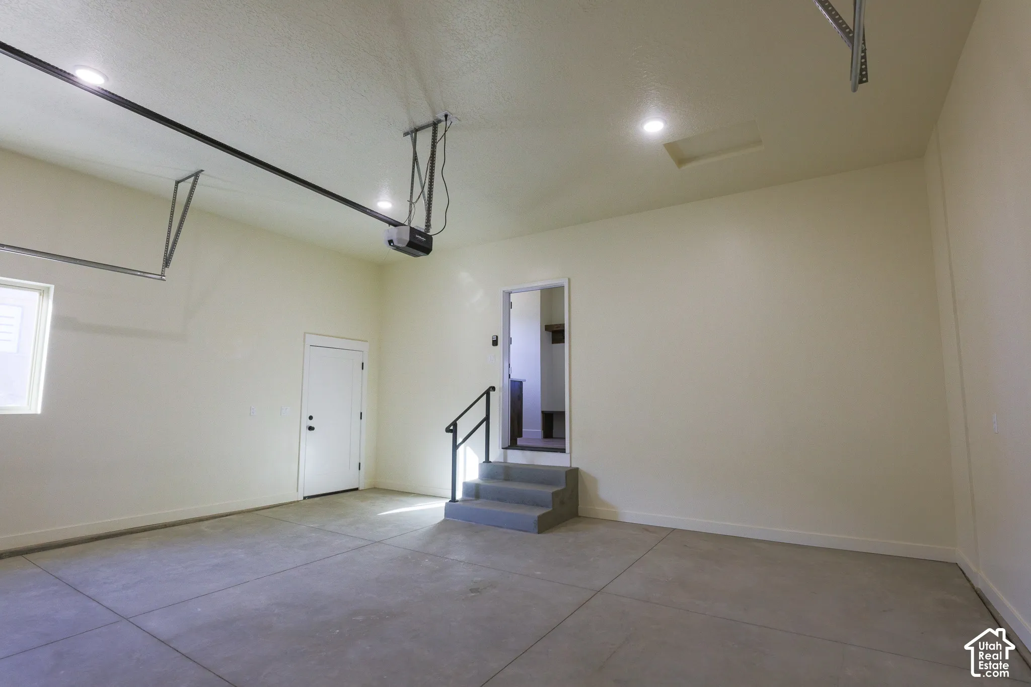 Finished garage featuring a concrete floor, recessed lighting, automated door opener, and a staircase with a handrail
