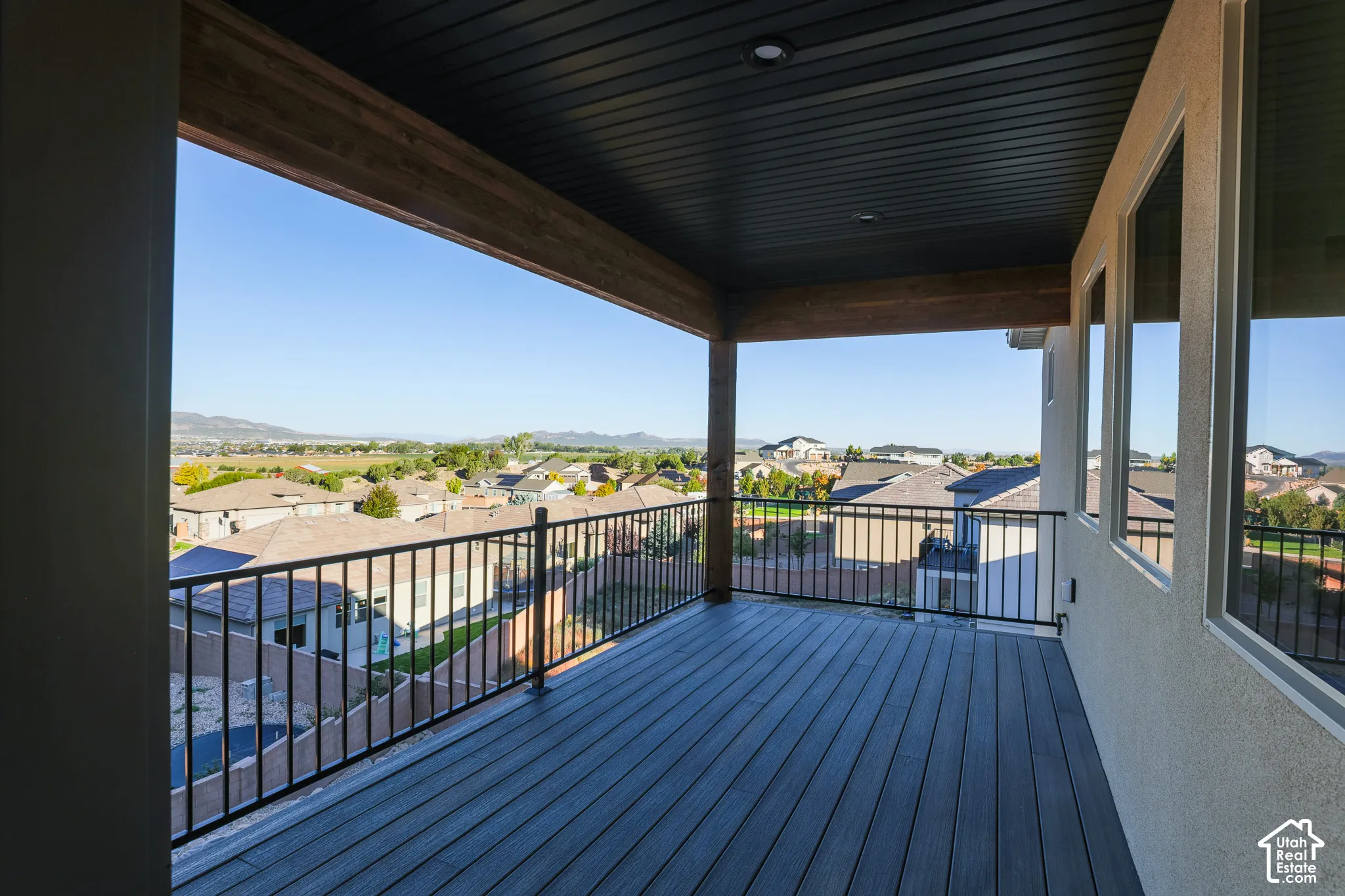 Covered balcony with composite decking, black metal railing, dark wood-tone soffit, and recessed lighting