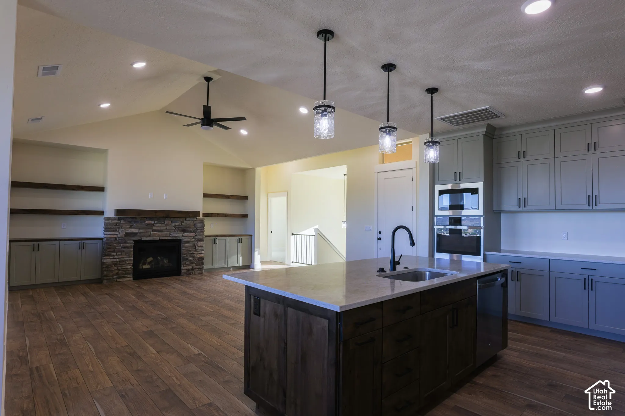 Vaulted ceiling, stone-surround fireplace with wood mantel, custom cabinetry, kitchen island with stone countertop, and wood-finish flooring