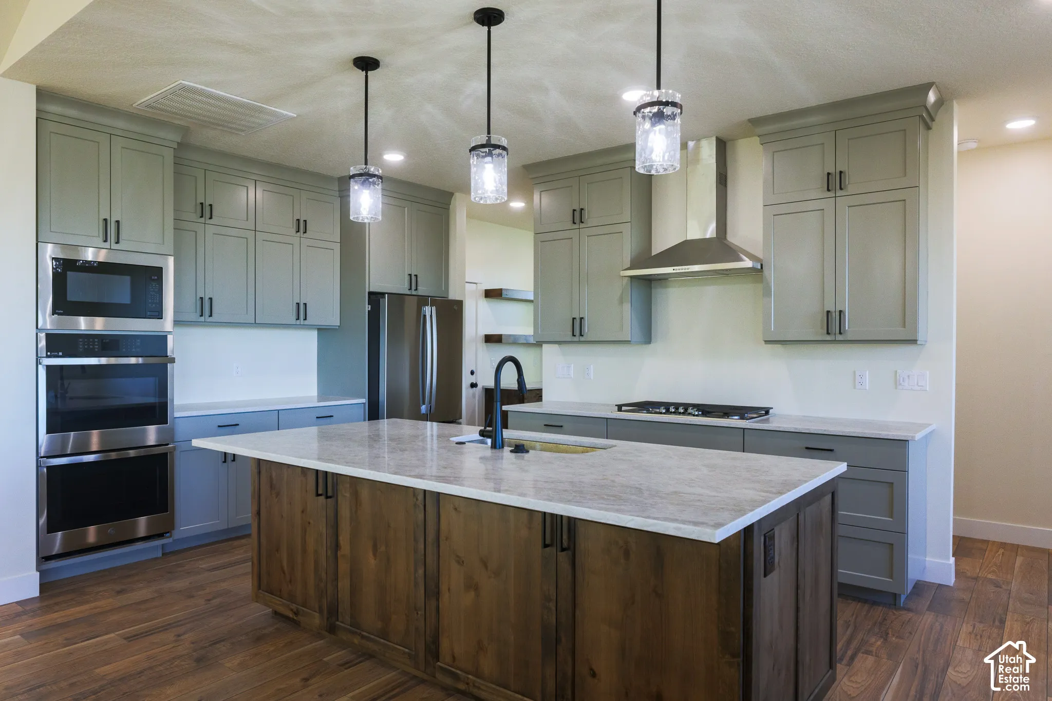 Kitchen featuring a large central island with wood cabinetry, quartz countertops, stainless steel wall-mounted double oven and microwave, custom pendant lighting, and neutral-toned cabinetry