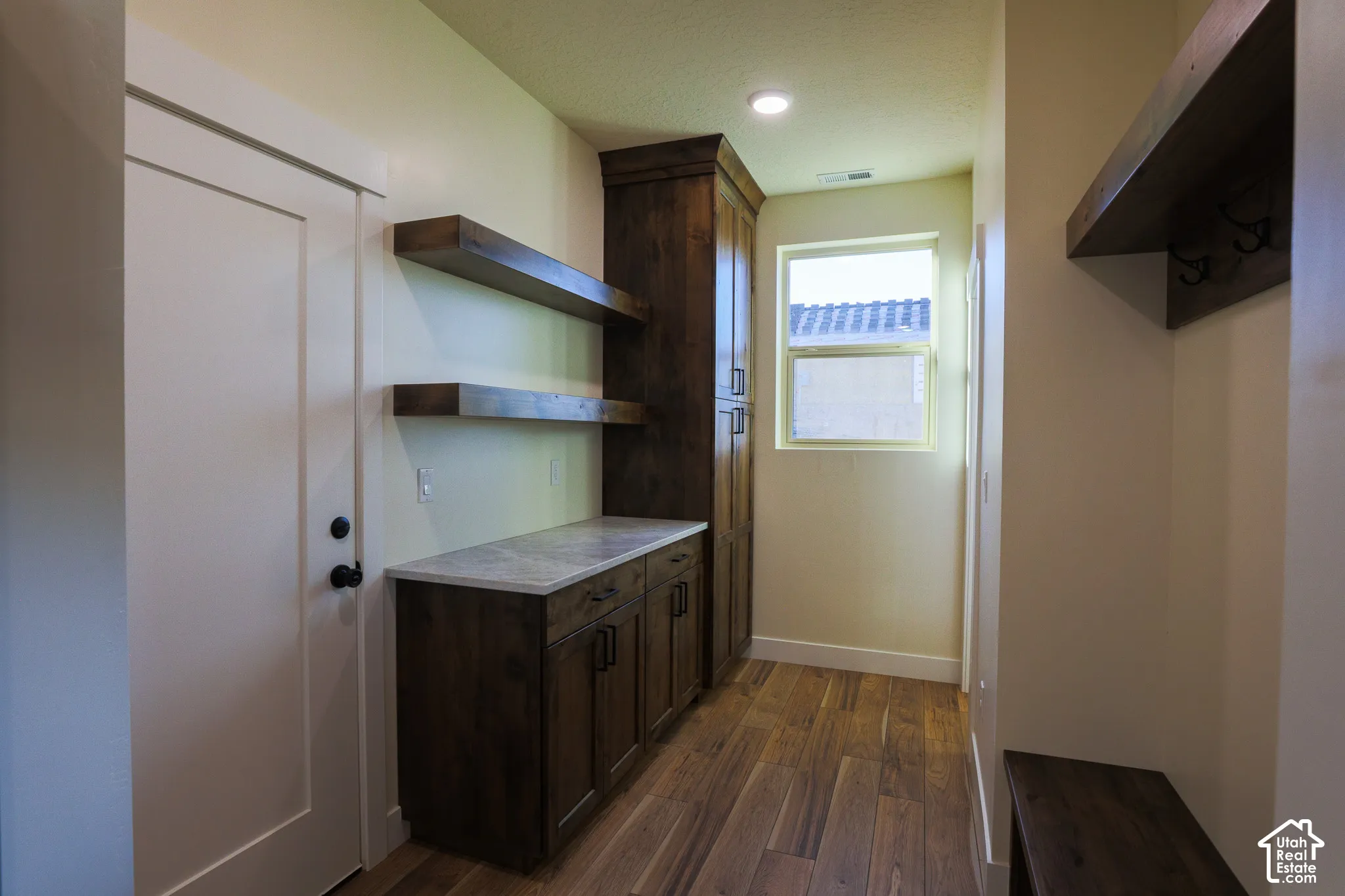 Wood-finish flooring, custom stained-wood cabinetry, stone-surface countertop, floating wood shelving, and integrated wood-finish bench seating