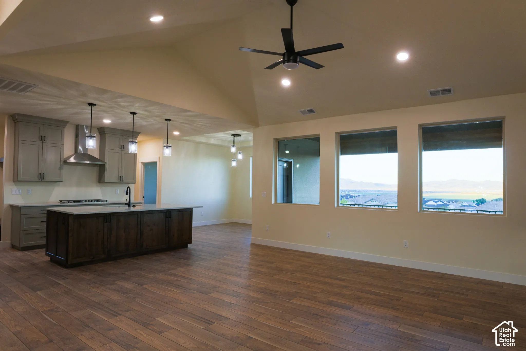 Vaulted ceilings with recessed lighting, wood-finish flooring, kitchen island with stone countertop, stainless steel range hood, and large windows with mountain and landscape scenery