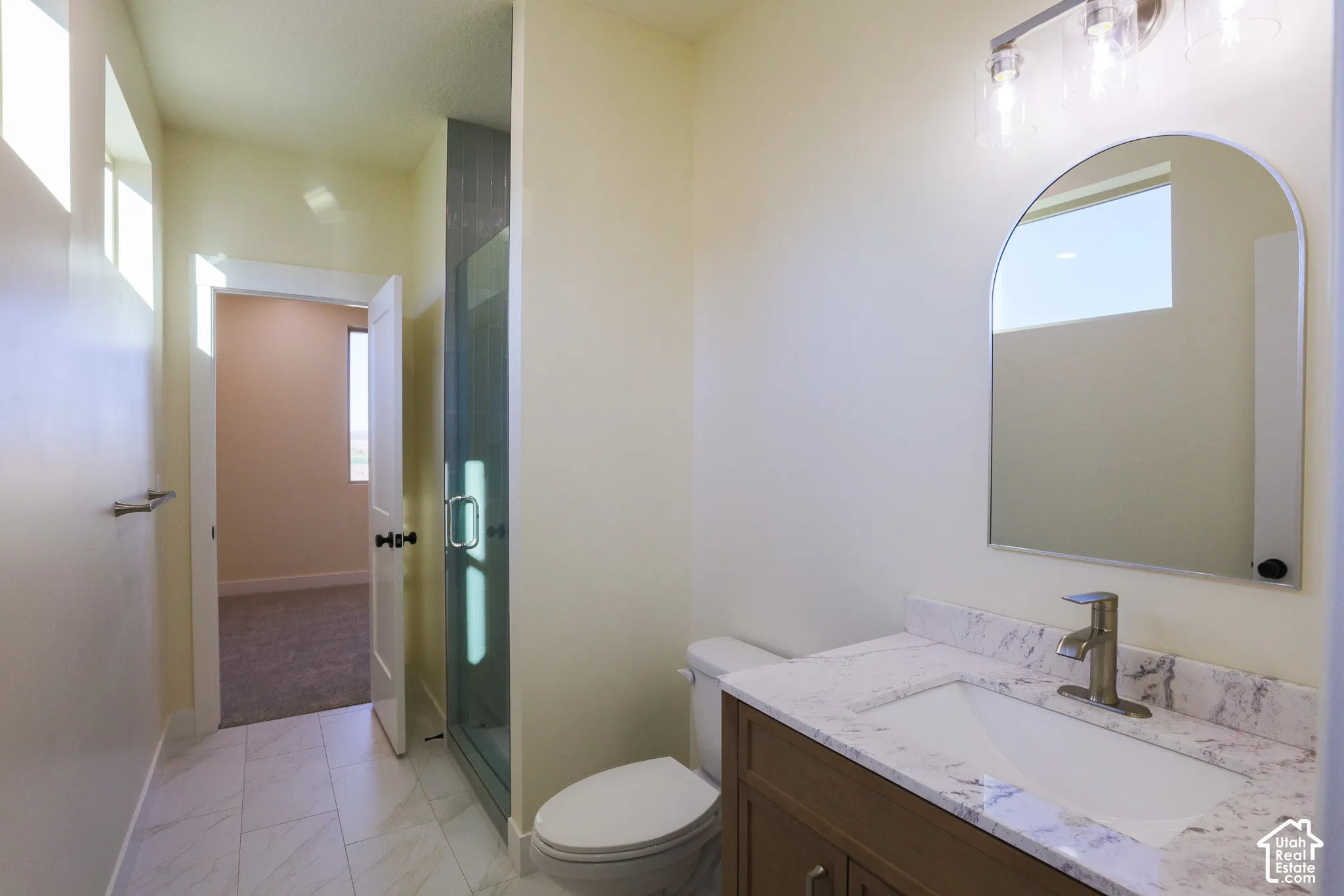 Bathroom featuring a vanity with a stone-finish countertop, undermount sink, arched mirror, glass-enclosed shower, and tile flooring