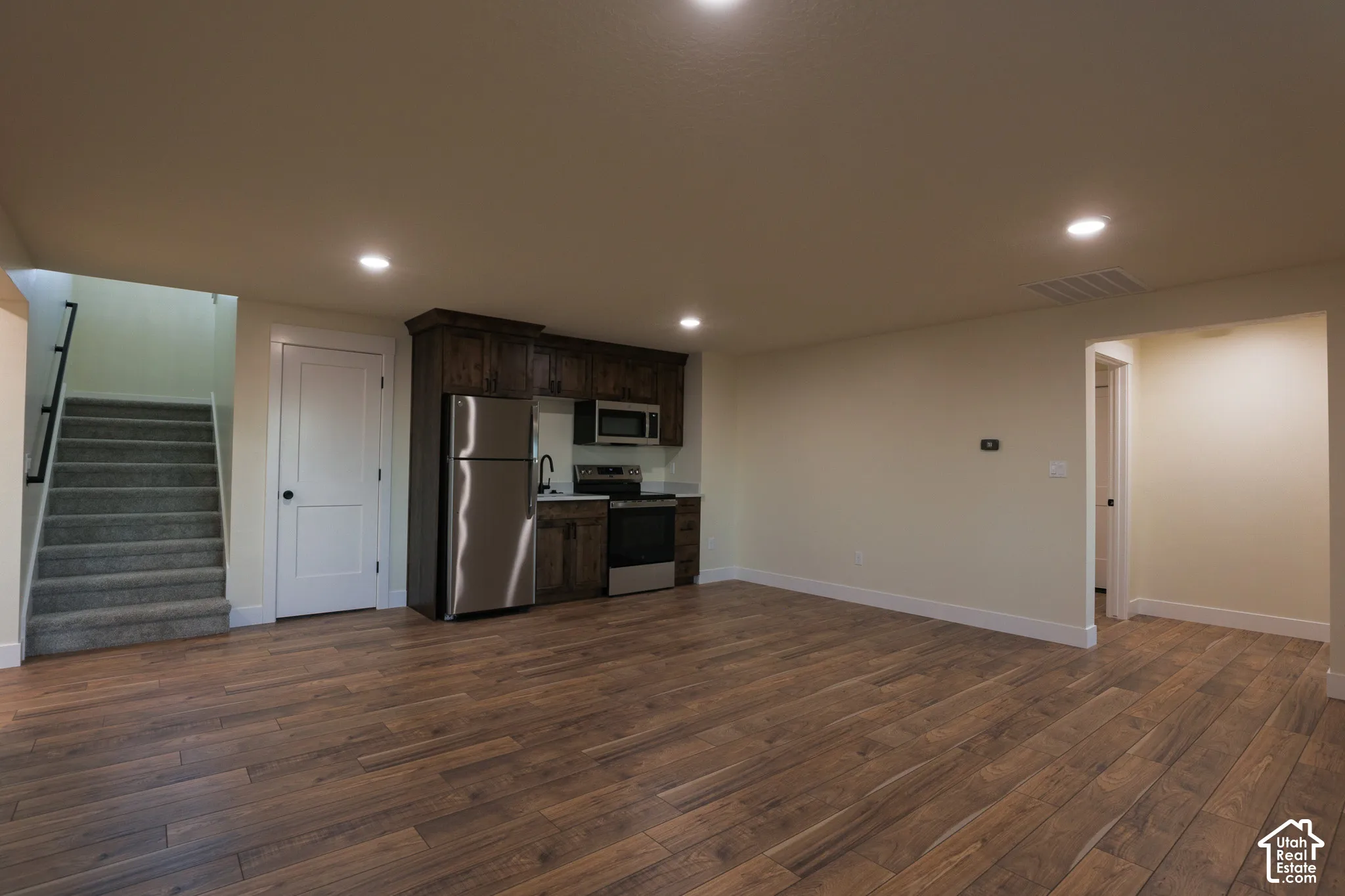 Kitchenette featuring dark-stained cabinetry, stainless steel appliances, and recessed lighting, finished with wood-finish flooring and carpeted staircase