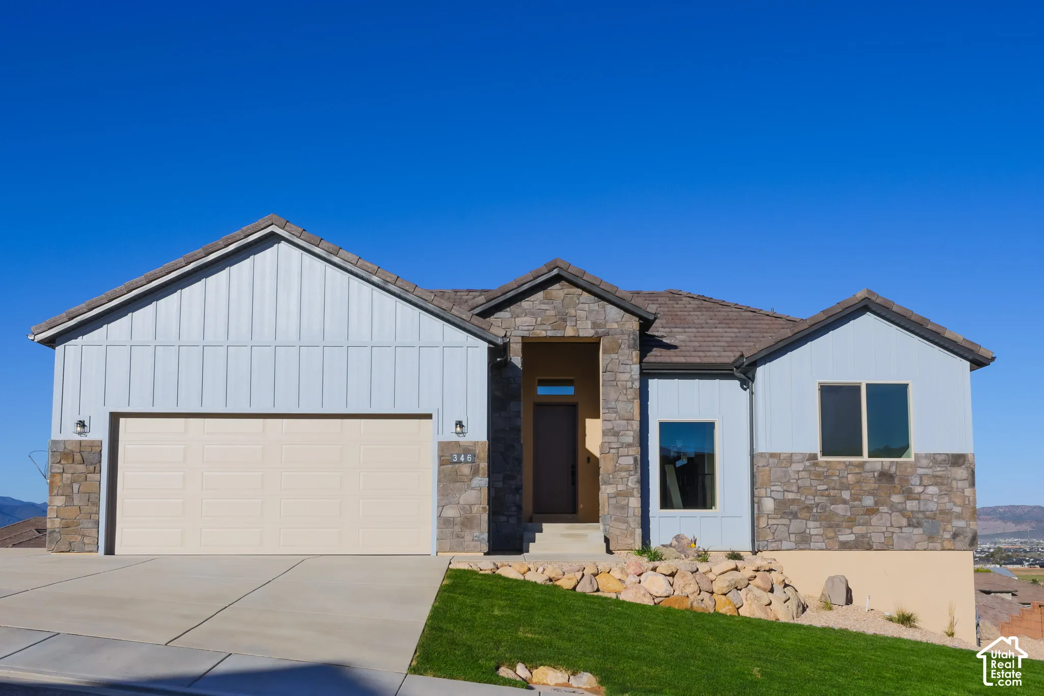 Exterior featuring board and batten siding, natural stone veneer accents, multi-slope rooflines, concrete driveway, and rock-based landscaping