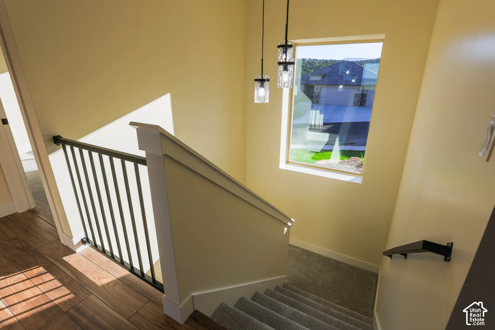 Staircase featuring wood-finish flooring, metal balusters, carpeted treads, wall-mounted handrail, and pendant light fixtures