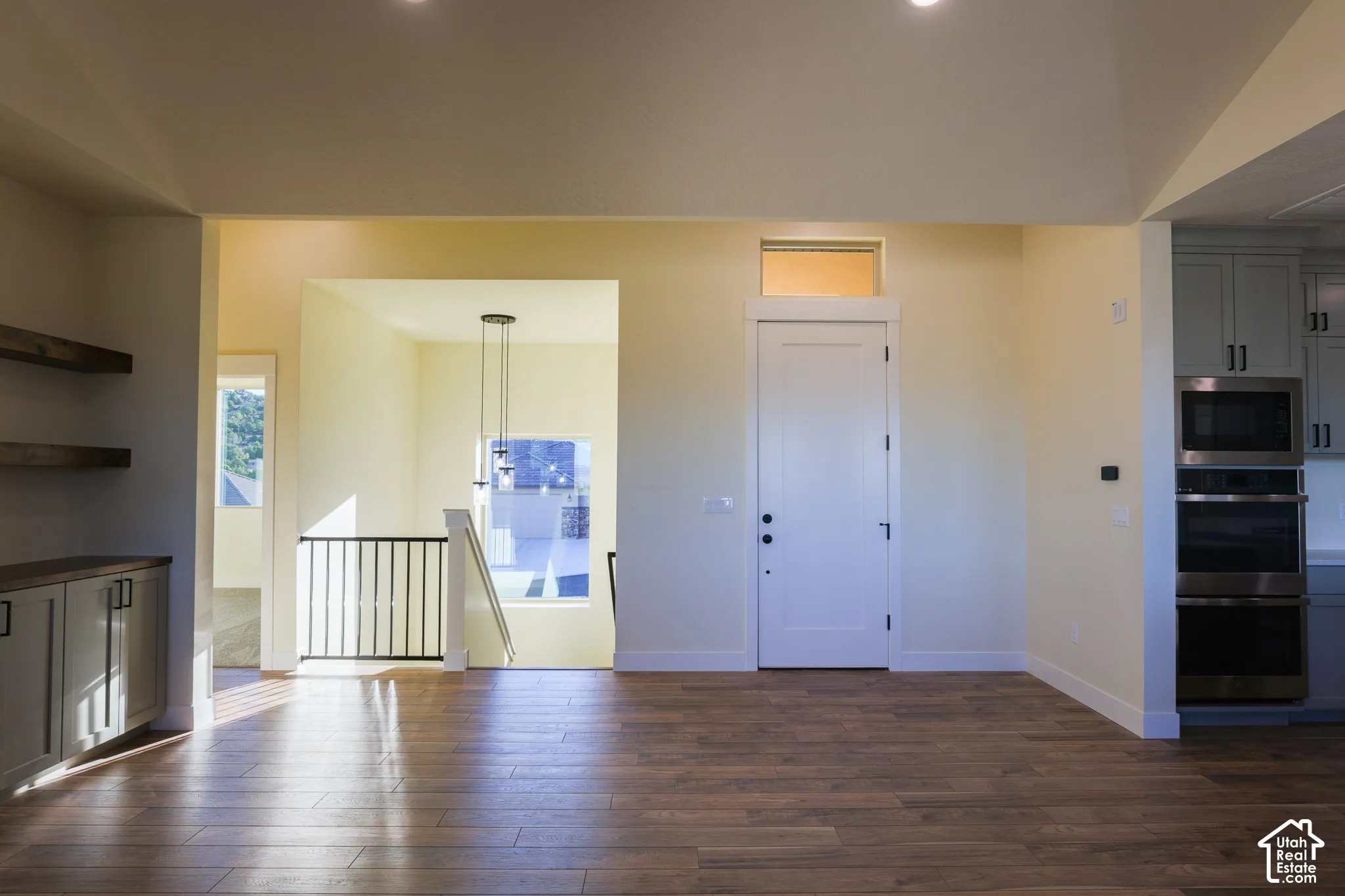 Vaulted ceilings, wood-finish flooring, built-in cabinetry with shelving, double wall-mounted ovens, and a staircase with metal balusters