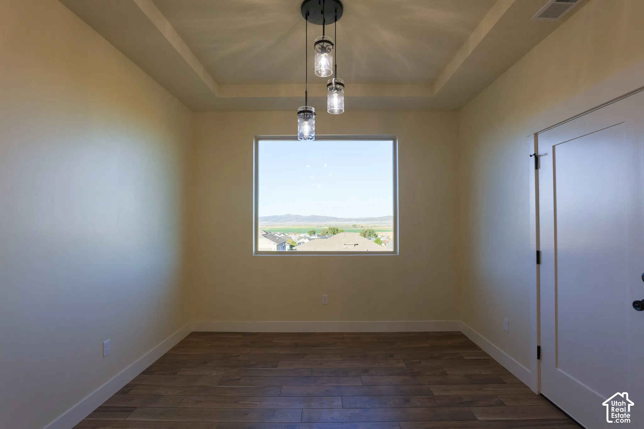 Room featuring a tray ceiling, wood-finish flooring, three-light jar pendant fixture, and a large window with mountain scenery