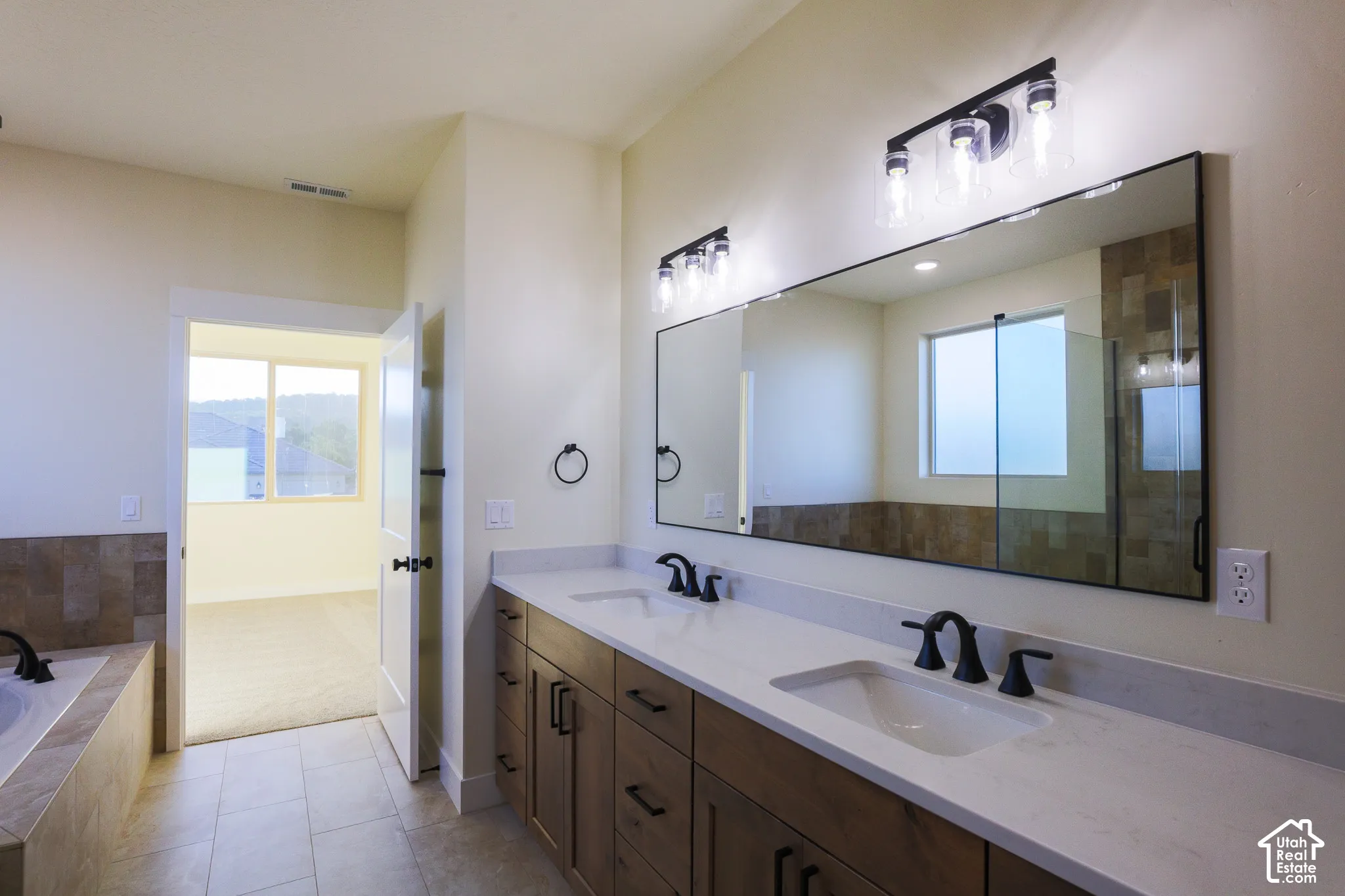 Dual-sink vanity with a solid-surface countertop, wood-finish cabinetry, matte black fixtures, and two modern multi-light wall sconces