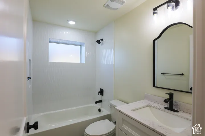 Bathroom featuring a vanity with a stone-patterned countertop, an arched-top mirror, matte black fixtures, and a tub enclosure with textured wall tile