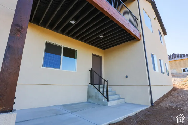 Covered concrete patio featuring a stucco exterior finish, recessed ceiling lighting, a wood-frame structural support beam, and metal stair railings