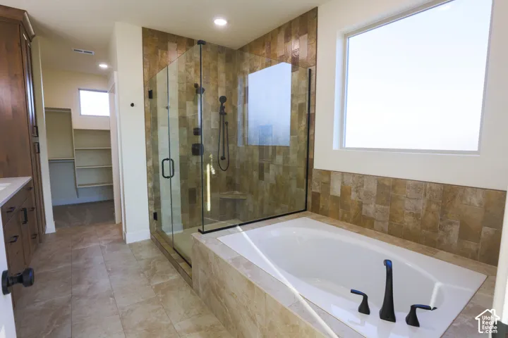 Glass-enclosed walk-in shower with textured stone-finish wall tile, drop-in soaking tub, tile flooring, and dark hardware finishes