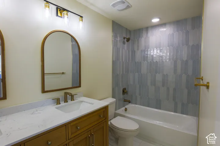 Bathroom featuring a vanity with a stone countertop, an arched mirror, three-light vanity fixture, and a tub surround with patterned vertical tile