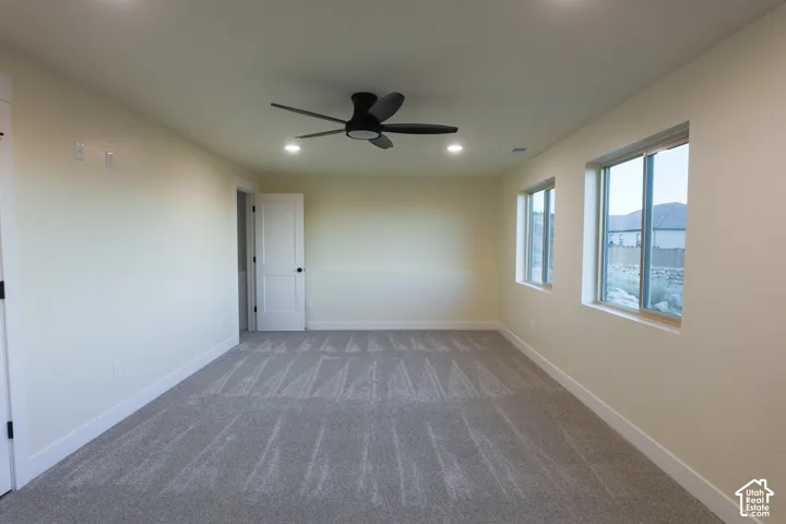 Neutral interior space featuring carpeted flooring, a ceiling fan with integrated lighting, recessed lighting, and multiple windows