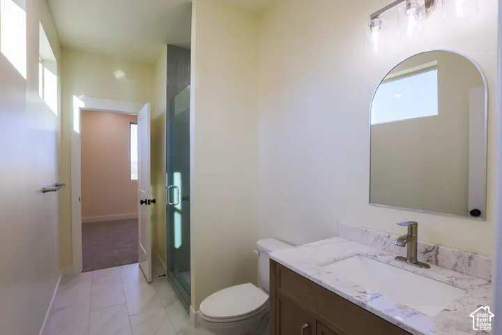 Bathroom featuring a vanity with a stone-finish countertop, undermount sink, arched mirror, glass-enclosed shower, and tile flooring