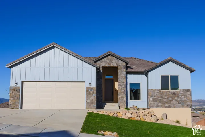 Exterior featuring board and batten siding, natural stone veneer accents, multi-slope rooflines, concrete driveway, and rock-based landscaping