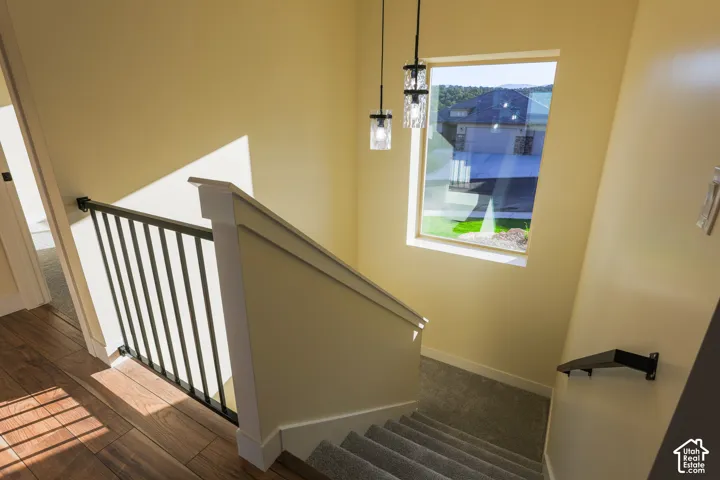 Staircase featuring wood-finish flooring, metal balusters, carpeted treads, wall-mounted handrail, and pendant light fixtures