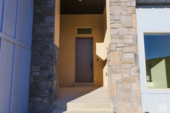 Covered entryway featuring stone-clad columns, vertical board-and-batten siding, a transom window, and a solid-panel door