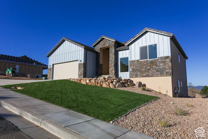Exterior featuring vertical siding, stone veneer accents, multi-gabled roofline, concrete driveway, and rock-based landscaping