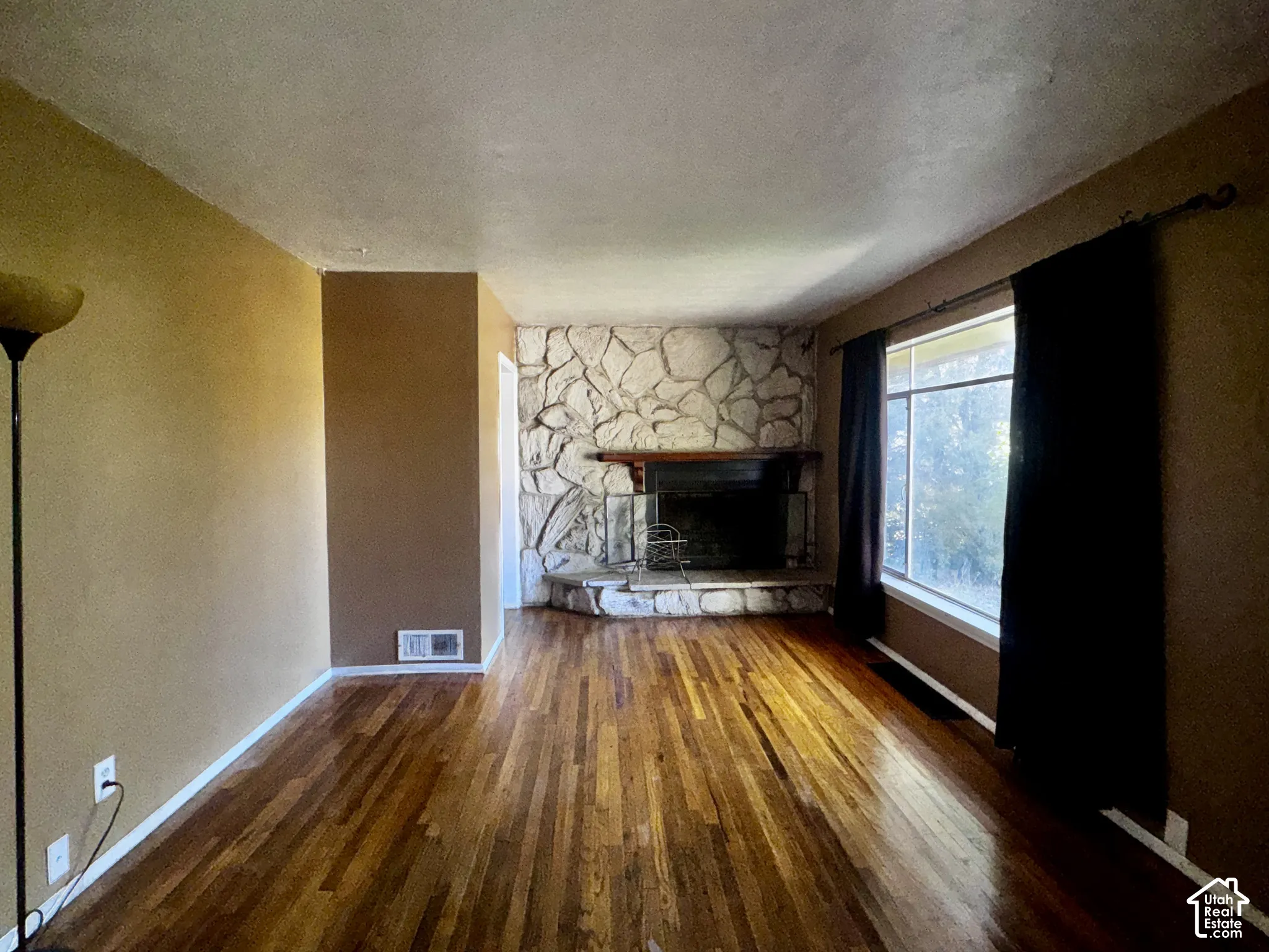 Living area featuring wood-finish flooring, floor-to-ceiling natural stone fireplace surround, raised stone hearth, and large window