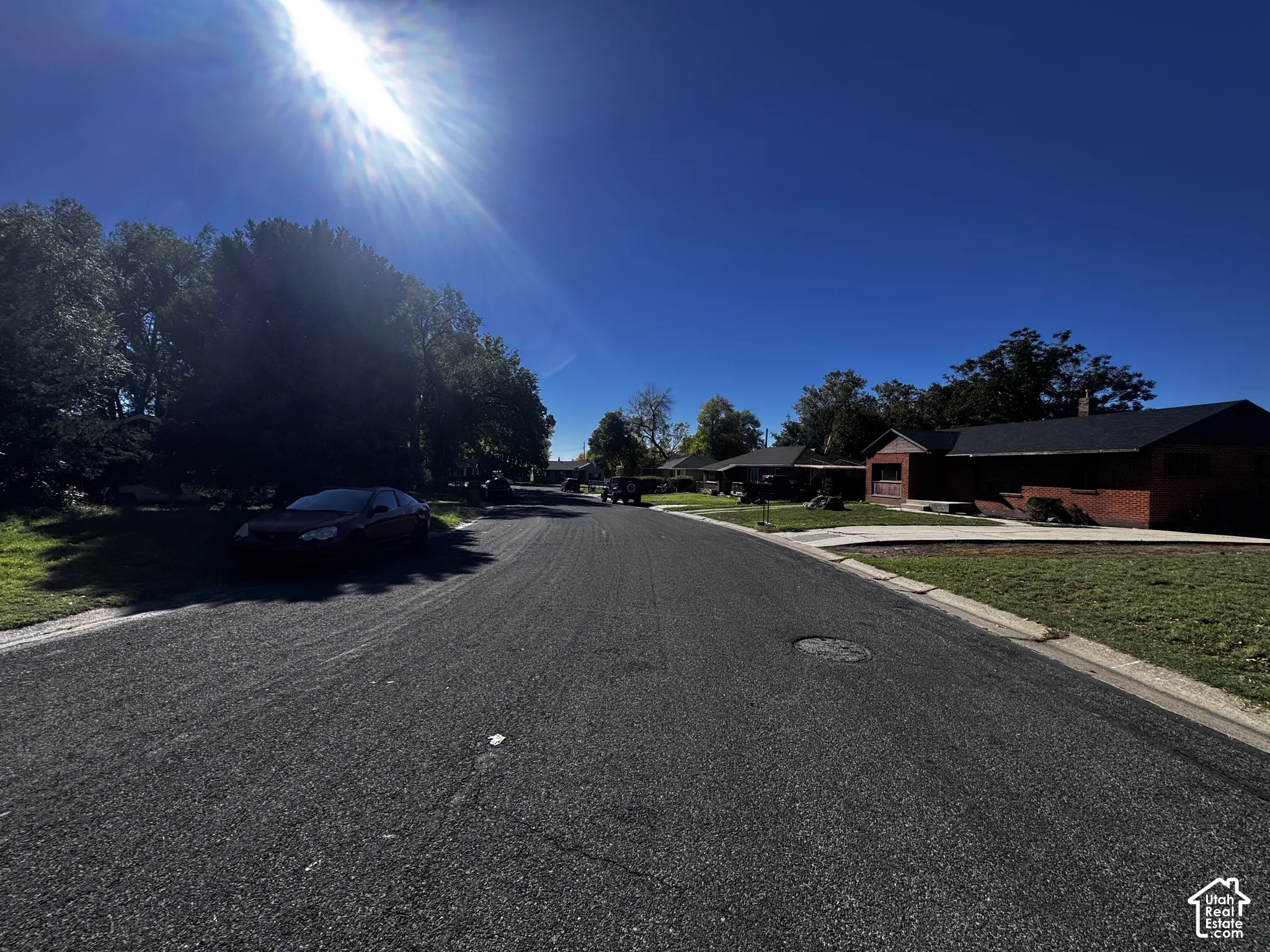 Residential street frontage featuring a red brick exterior, mature trees, and concrete curbing