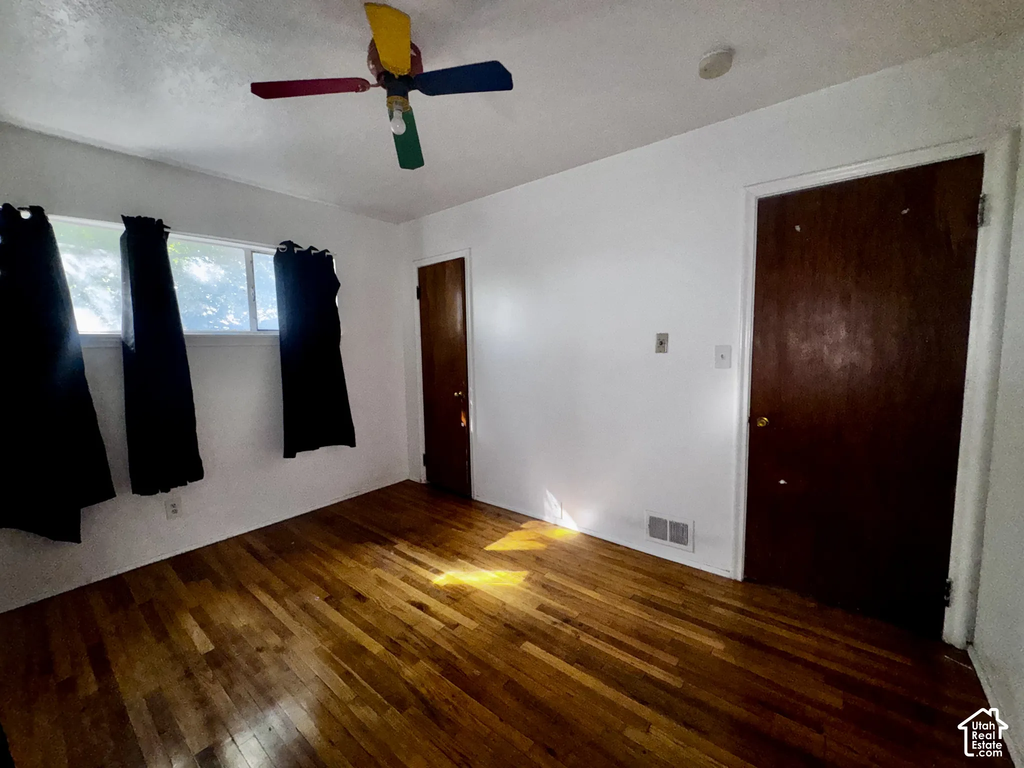 Room featuring wood-finish flooring, a multi-colored ceiling fan, and solid wood-finish interior doors