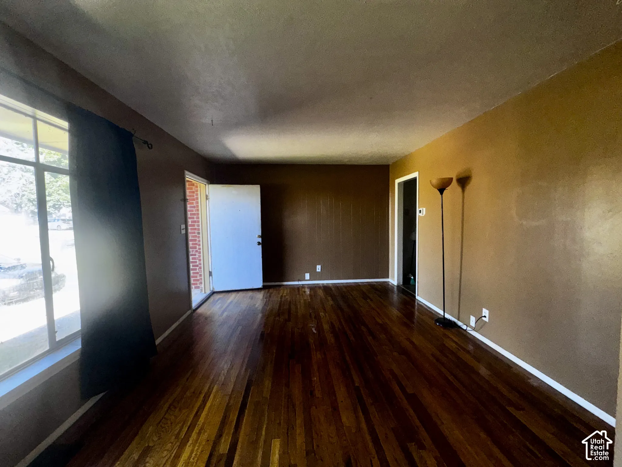 Interior space featuring wood-finish flooring, a large window with multi-pane configuration, and exterior brick wall detailing visible through the doorway