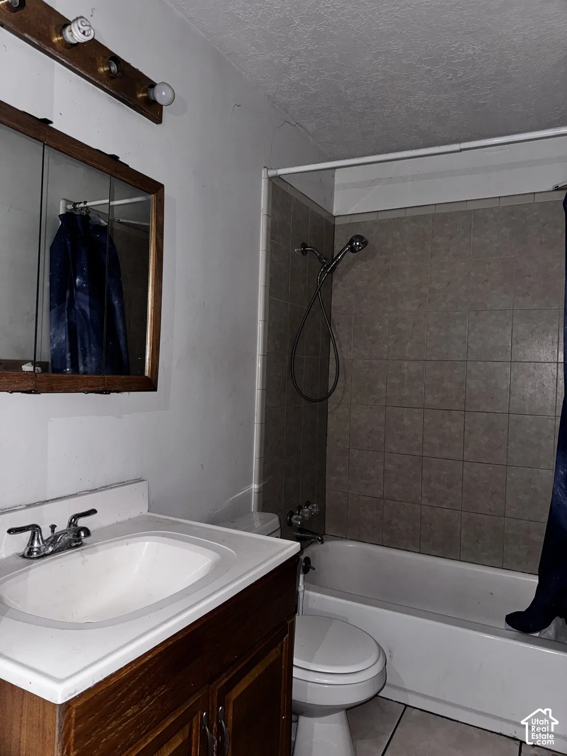 Bathroom featuring a wood vanity with an integrated basin, wall-mounted medicine cabinet, multi-bulb vanity light, and a tile-surround shower and tub combination