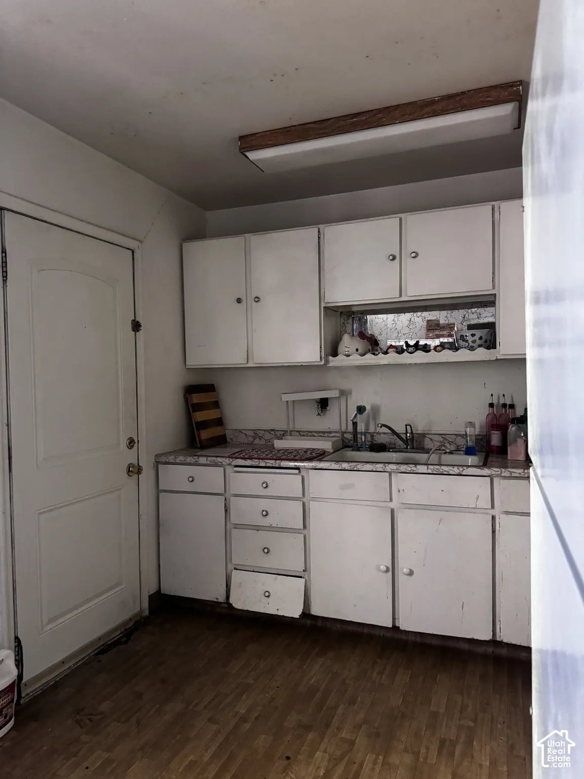 Kitchen featuring white cabinetry, patterned laminate countertops, a stainless steel sink with a chrome faucet, and wood-finish flooring