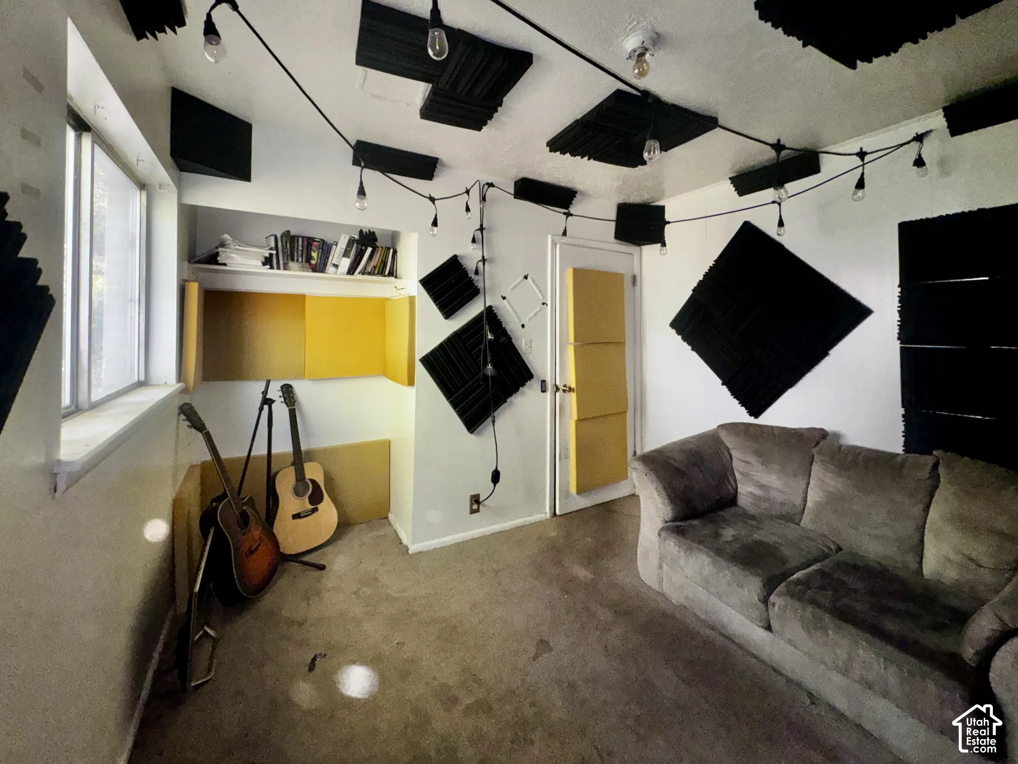 Room featuring wall-mounted acoustic treatment panels, recessed built-in shelving, carpeted flooring, and a single-pane window