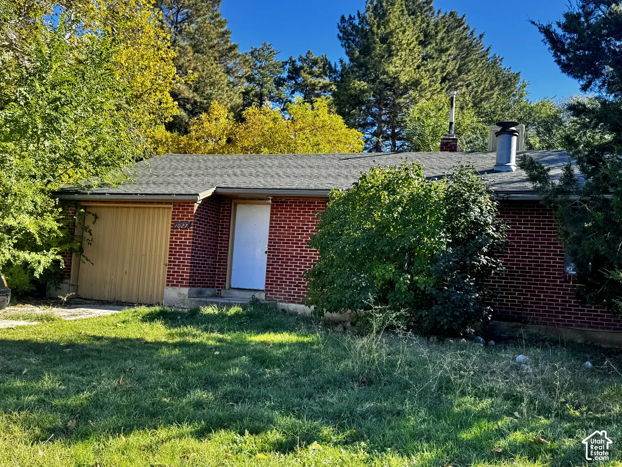 Single-story residence featuring a red brick exterior, attached garage, shingled roof, and dual exterior chimneys