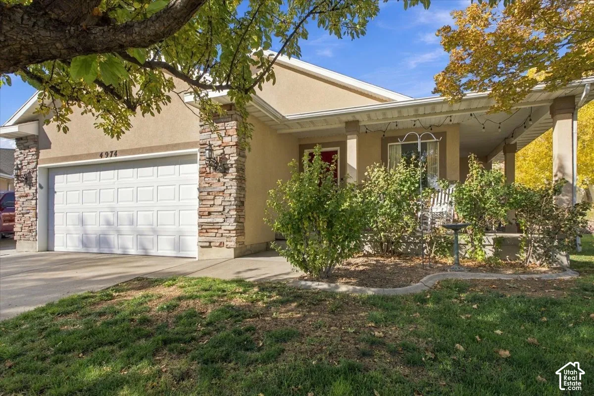Single-story exterior featuring a stone-veneer accent wall, stucco facade, covered front porch, and a two-car garage