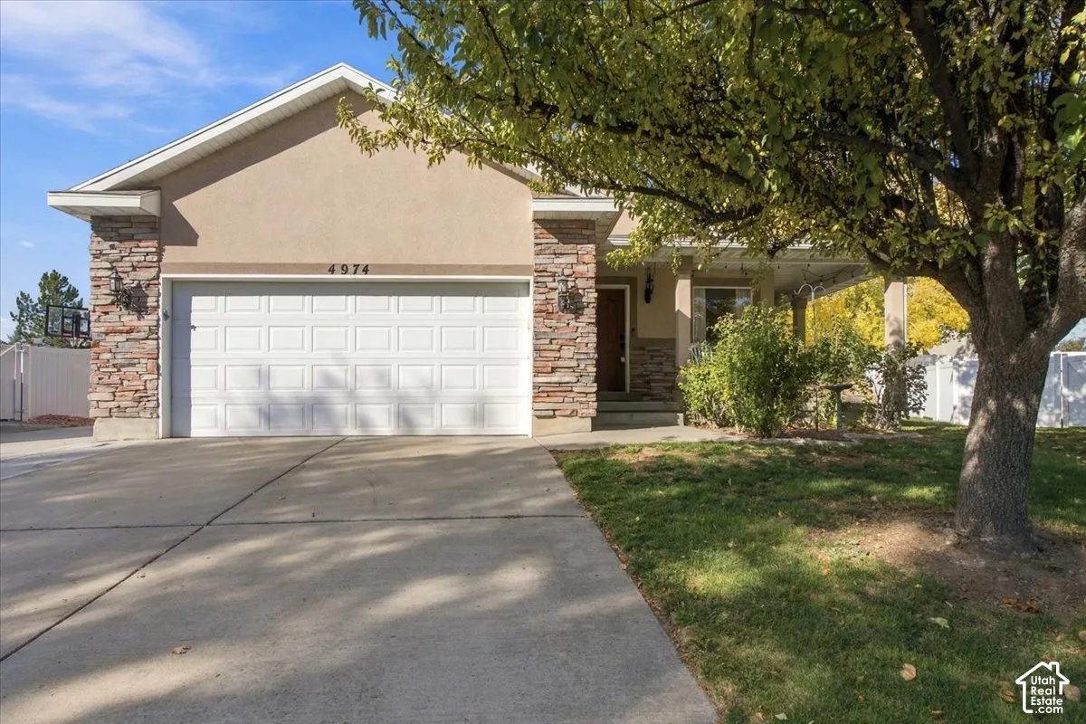 Single-story exterior featuring a concrete driveway, two-car garage, stone veneer accents, and a covered entryway