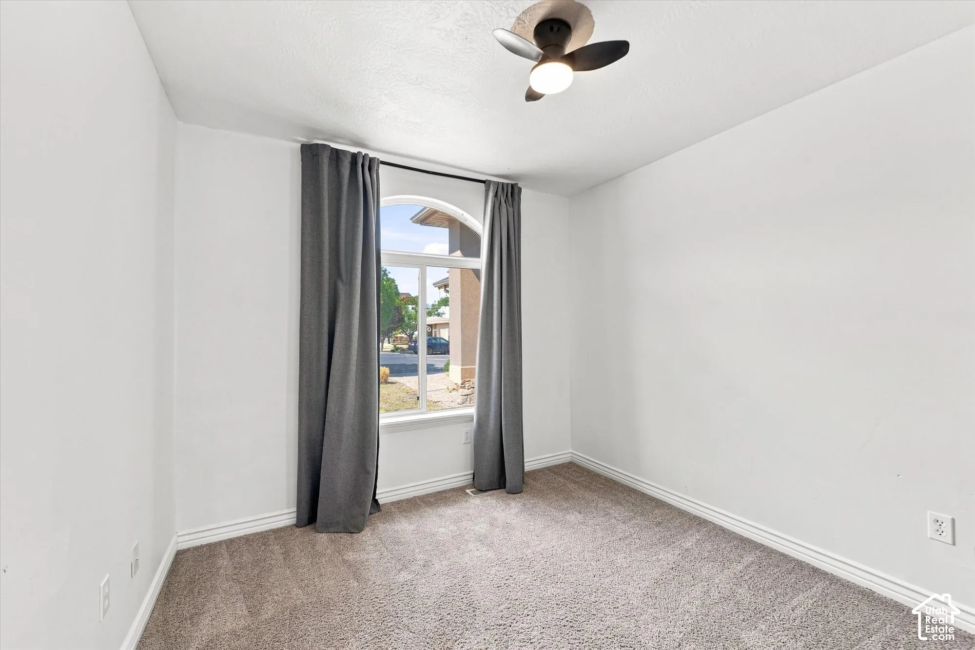 Neutral-toned room featuring plush carpeting, an arched window, and a contemporary ceiling fan with integrated lighting