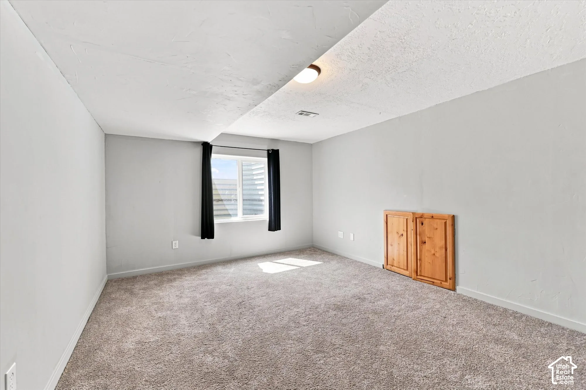 Neutral-toned interior space featuring wall-to-wall carpeting, a single-pane window, and built-in wood-panel access doors