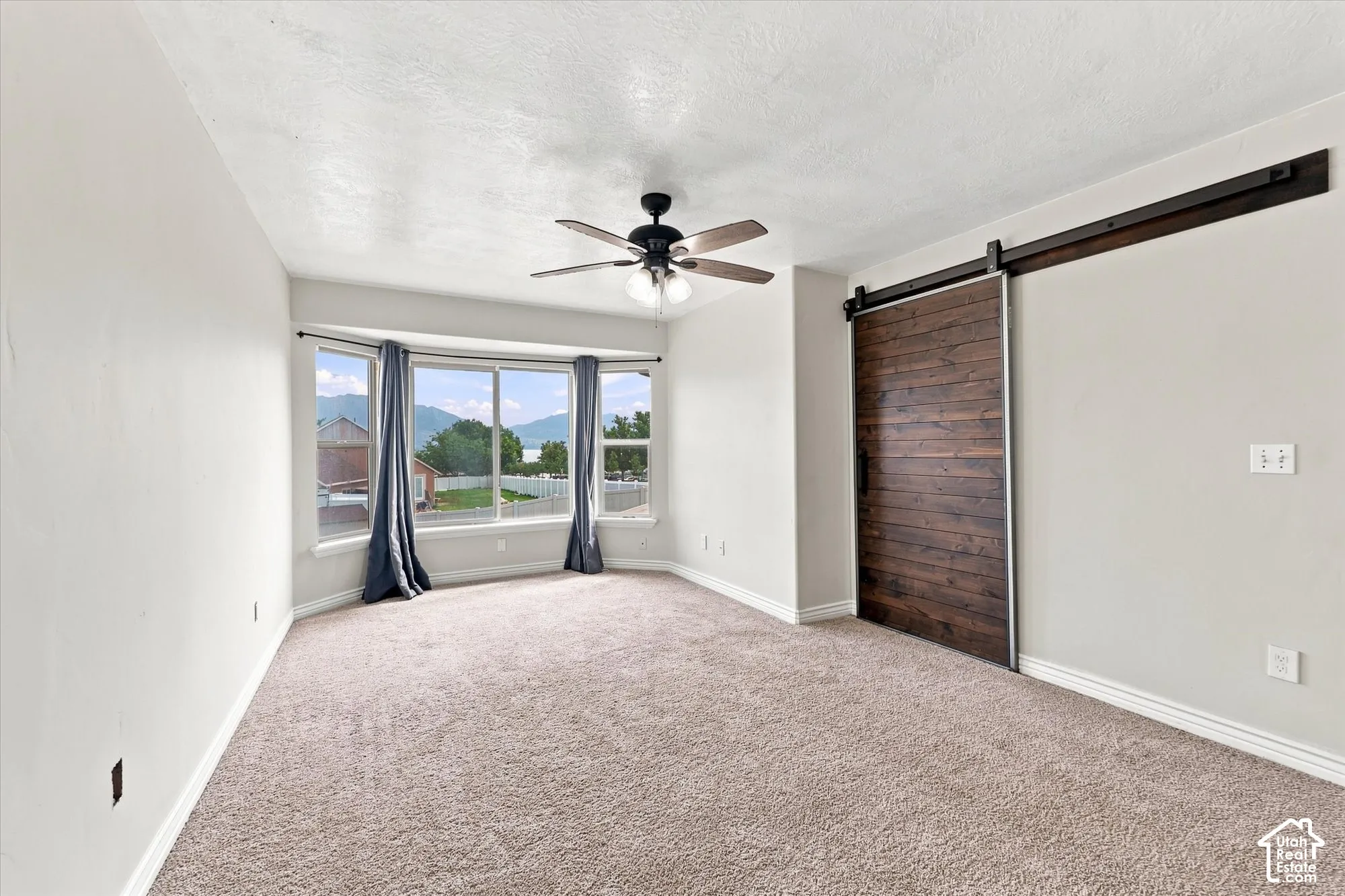 Room featuring a bay window, wood-finish sliding barn door, and a ceiling fan with integrated lighting