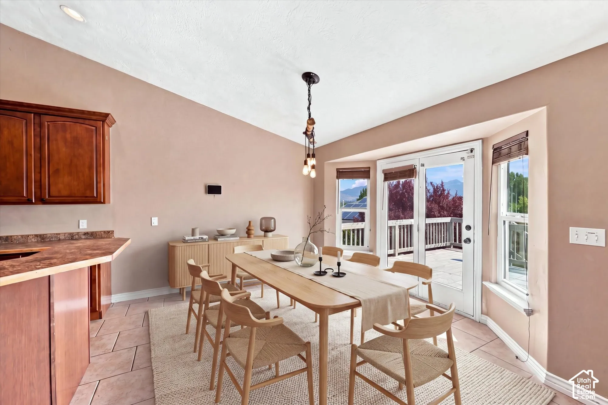 Vaulted ceiling, natural stone flooring, dark wood cabinetry, multi-light pendant fixture, and double glass doors opening to a deck