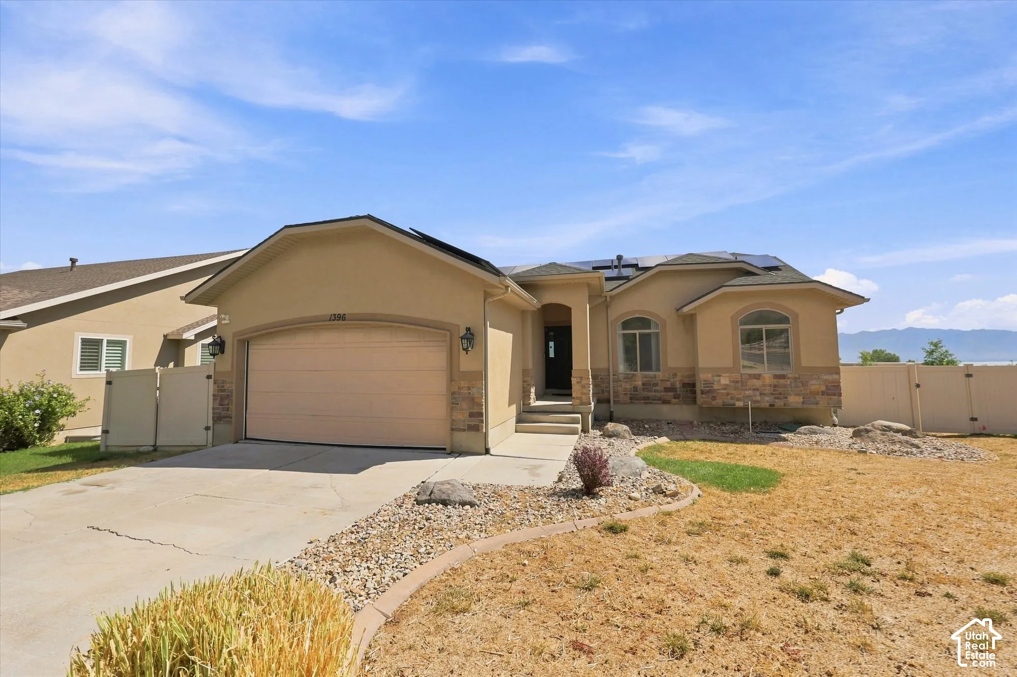 Stucco exterior with stone veneer accents, attached two-car garage, roof-mounted solar panels, and arched window detailing