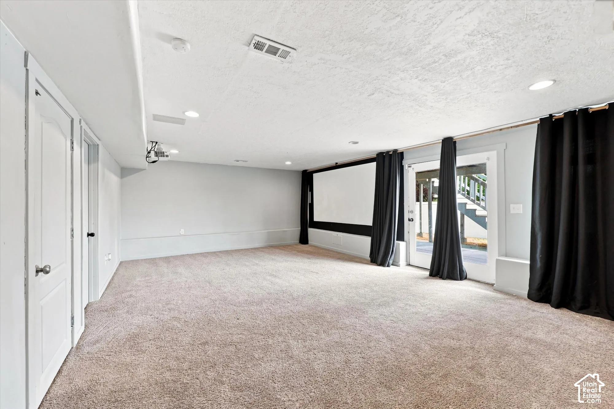Spacious room featuring neutral carpeting, recessed lighting, a mounted projector, a wall-integrated screen, and glass-paned double doors with exterior access
