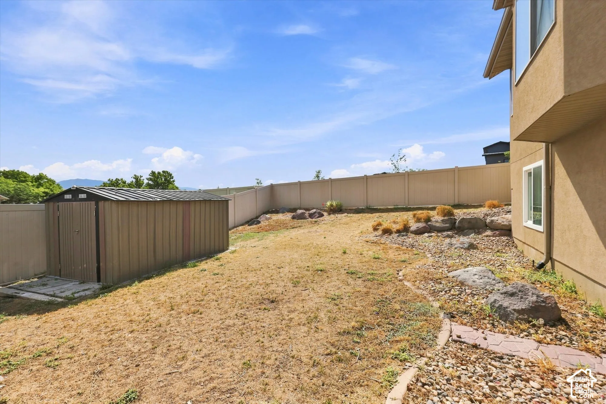 Rear yard featuring a metal storage shed, tan vinyl perimeter fencing, and stone landscape elements
