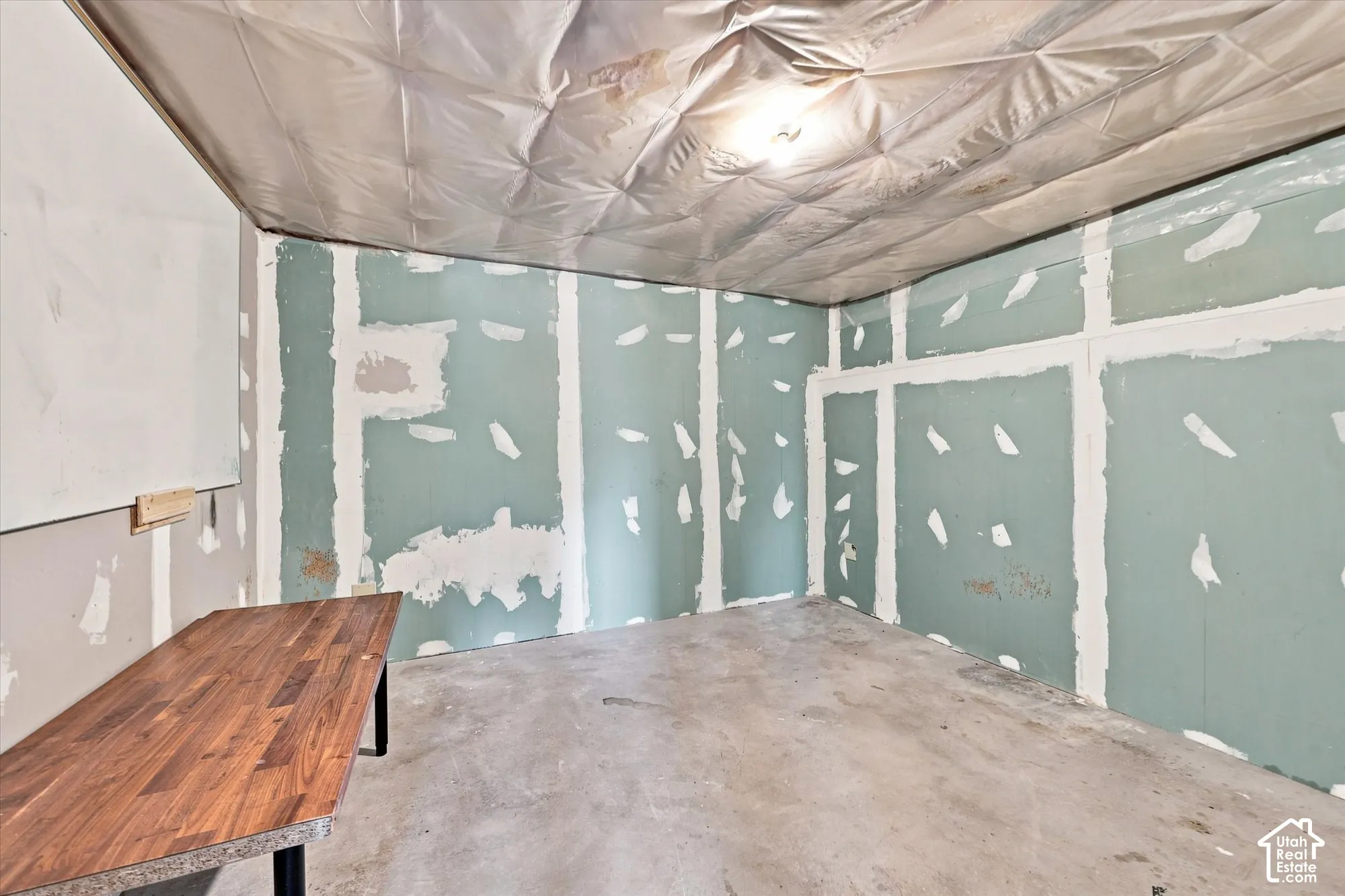 Unfinished interior space featuring exposed drywall, concrete flooring, and a vapor barrier ceiling treatment