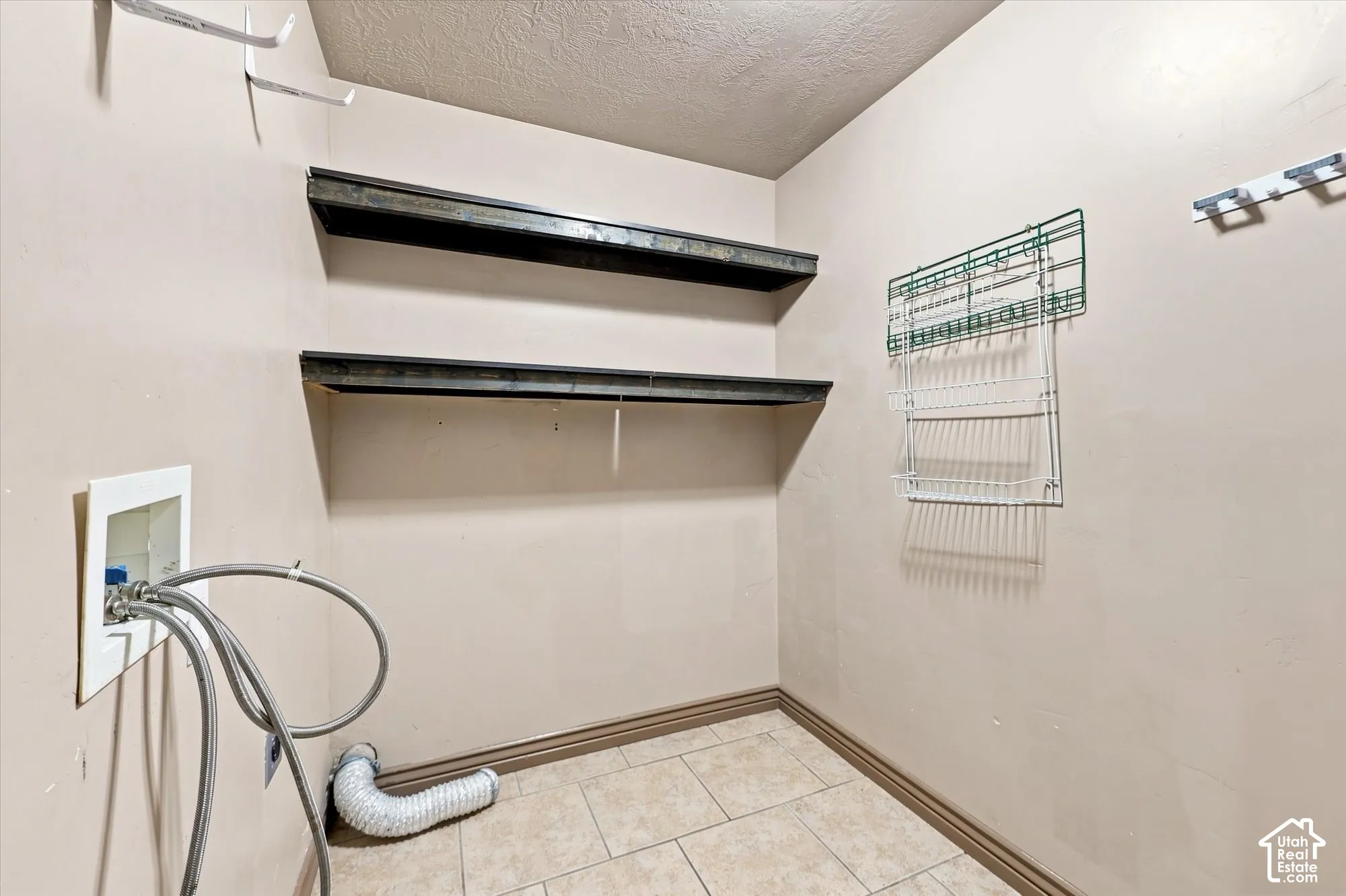 Utility space featuring ceramic tile flooring, dual metal wall-mounted shelving units, and dedicated plumbing connections