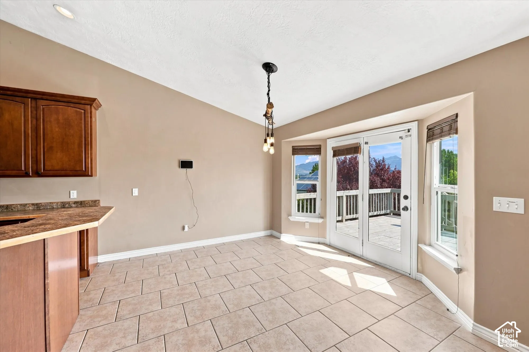 Vaulted ceilings, tile flooring, custom cabinetry, multi-light pendant fixture, and French doors leading to a wooden deck