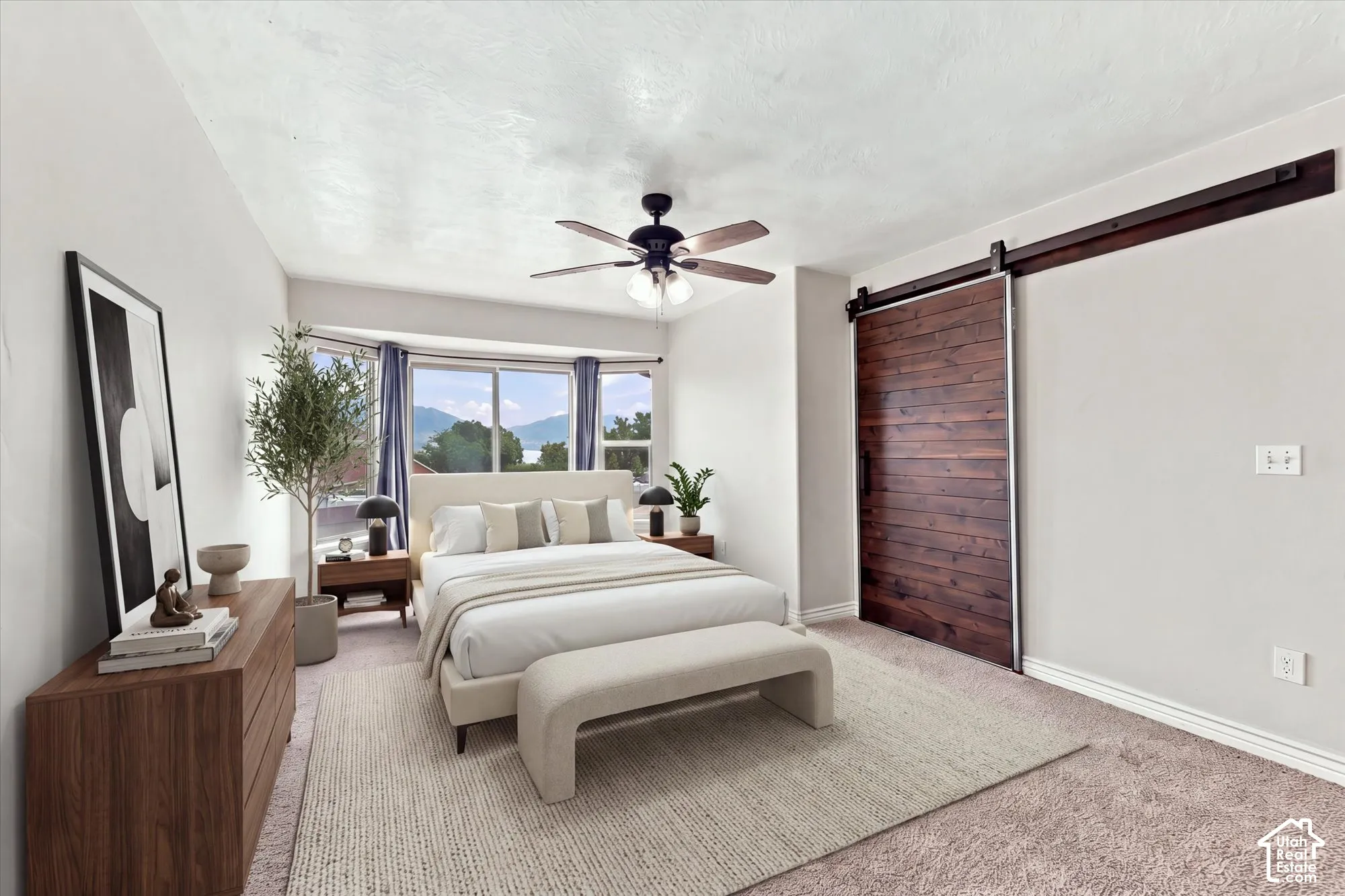 Interior space featuring a wooden sliding barn door, bay window with mountain backdrop, and ceiling-mounted fan with integrated lighting