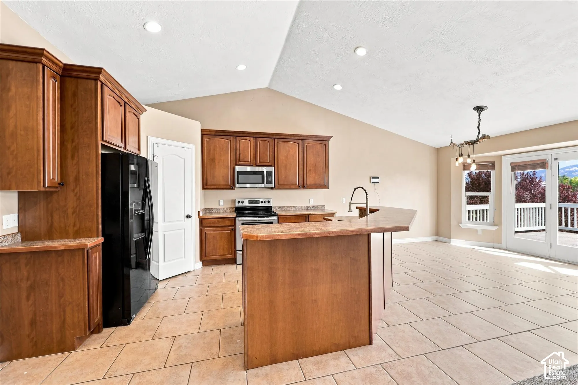 Kitchen featuring wood cabinetry, solid surface countertops, tile flooring, vaulted ceilings, and recessed lighting